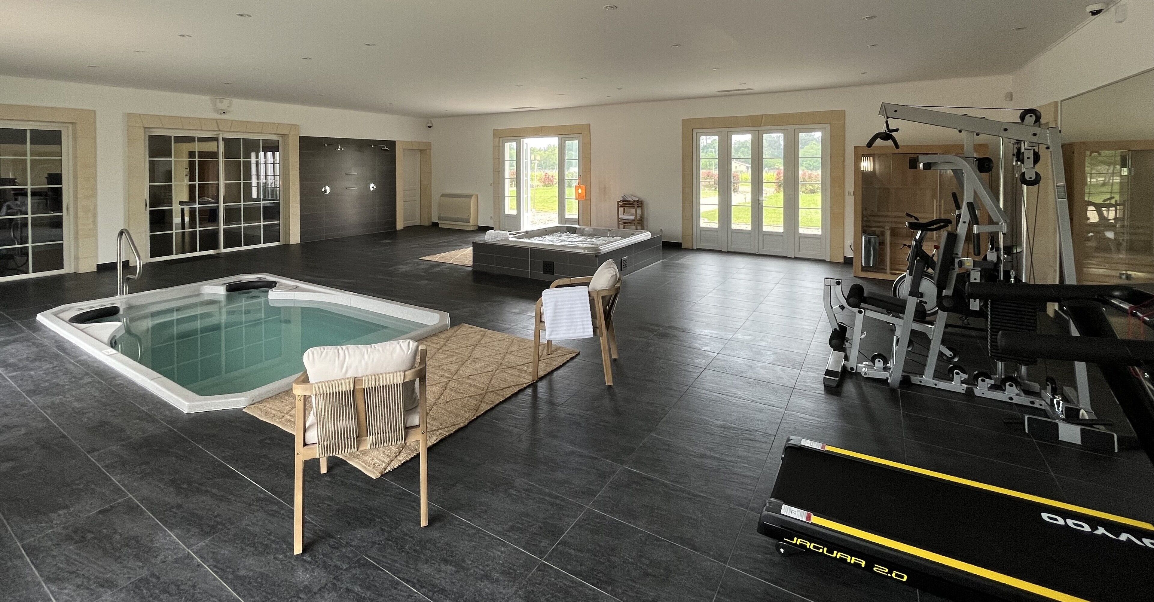 Un espace intérieur spacieux comprenant un jacuzzi, du matériel d’exercice et une grande fenêtre offrant une vue sur l’extérieur.