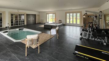 Un espace intérieur spacieux comprenant un jacuzzi, du matériel d’exercice et une grande fenêtre offrant une vue sur l’extérieur.