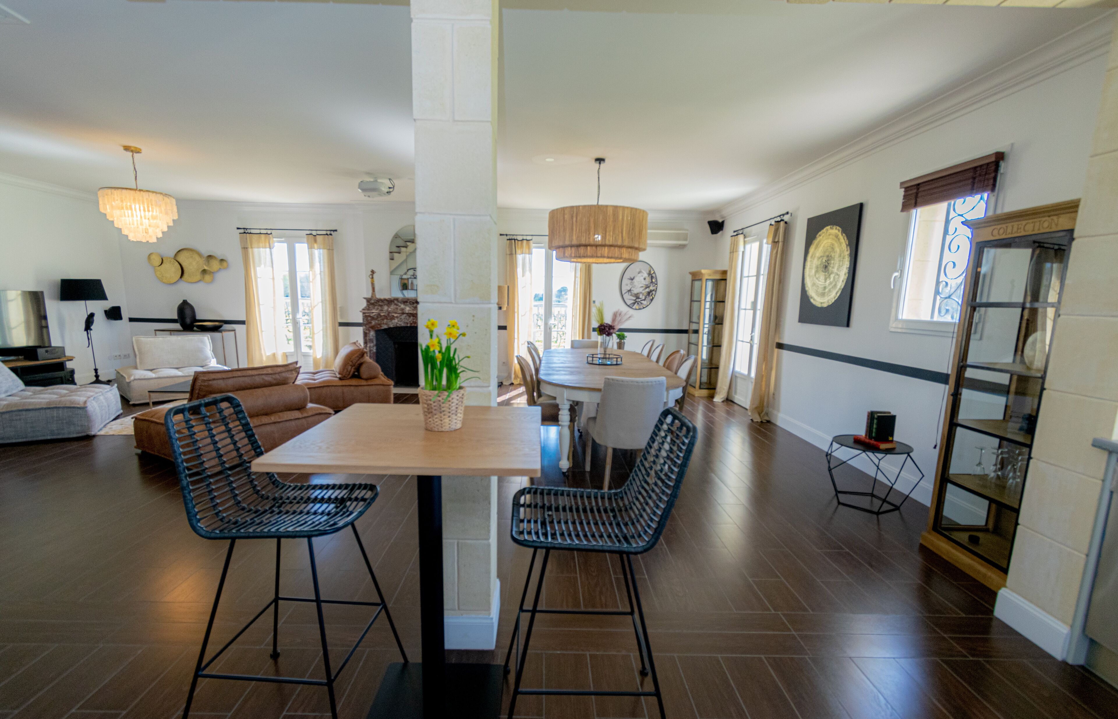 Un salon spacieux avec un coin repas, comprenant une grande table en bois, deux tabourets de bar et un canapé.