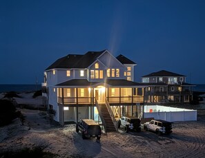 A large, multi-story beachfront house with a covered front porch, multiple windows, and a visible garage. - Memories | 4BR Swan Beach 4x4 OBX | New Pool & Hot Tub | Sleeps 9 (Corolla)