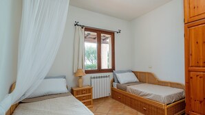 Une chambre avec deux lits simples, une fenêtre avec un rideau, une table de chevet avec une lampe et une armoire en bois.