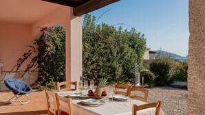Un espace de restauration en plein air avec une table dressée pour quatre personnes, entourée de chaises en bois, sous une pergola.