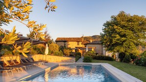 A swimming pool with lounge chairs, a stone wall, and a building with a tiled roof in the background. - Grano - Casa Bella Vista (Force)