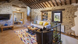 A rustic stone interior with a wooden ceiling, a sofa with cushions, a coffee table, a TV, and a bookshelf. - Grano - Casa Bella Vista (Force)