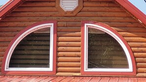 Une cabane en rondins de bois, dotée de deux fenêtres en arc de cercle et d’un toit rouge.