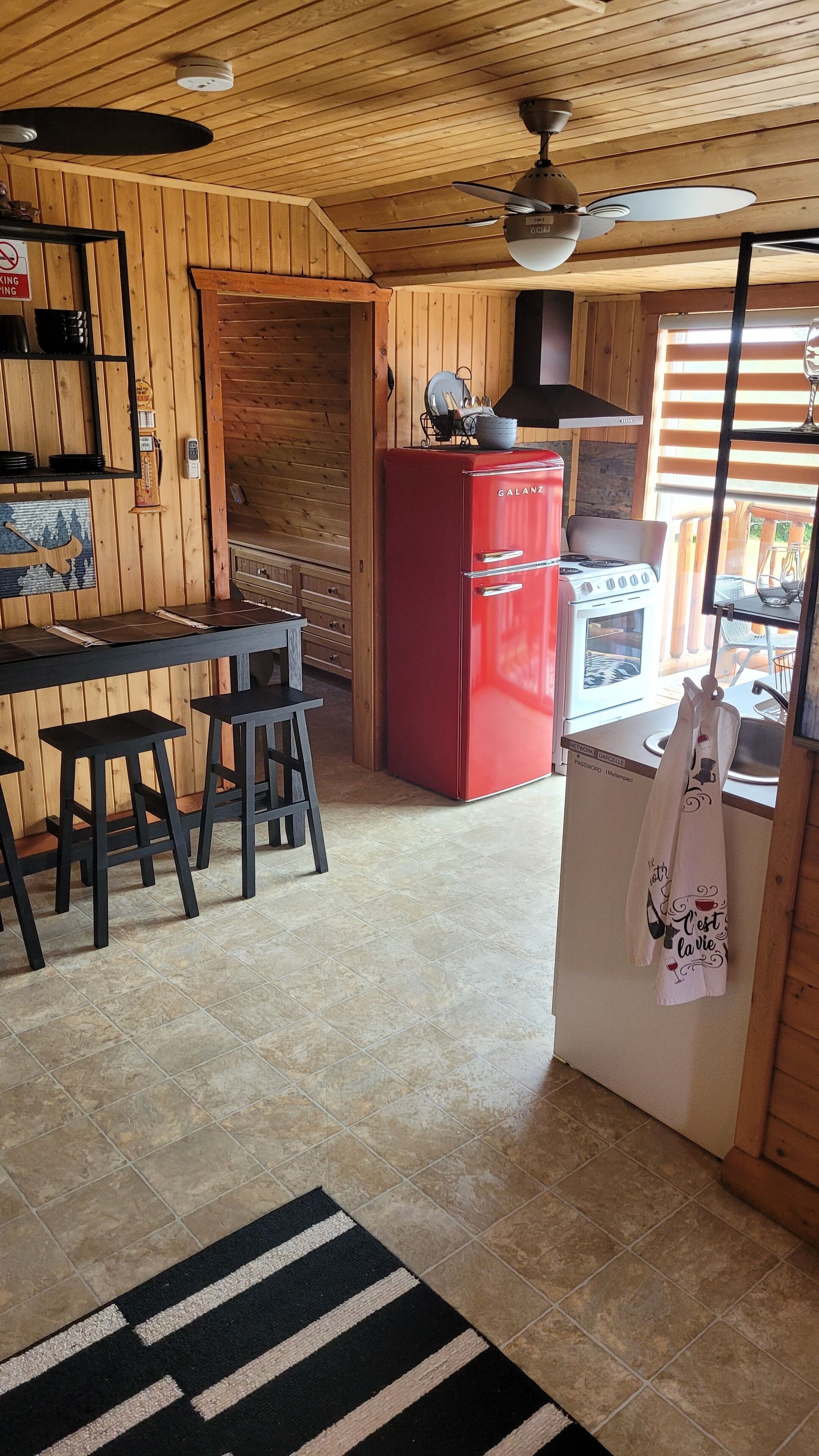 Eine kleine Küche mit Holzwänden, einem roten Kühlschrank, einem Gasherd und einem Deckenventilator.