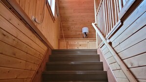Un escalier en bois avec une rampe, menant à un palier doté d’un luminaire au plafond.