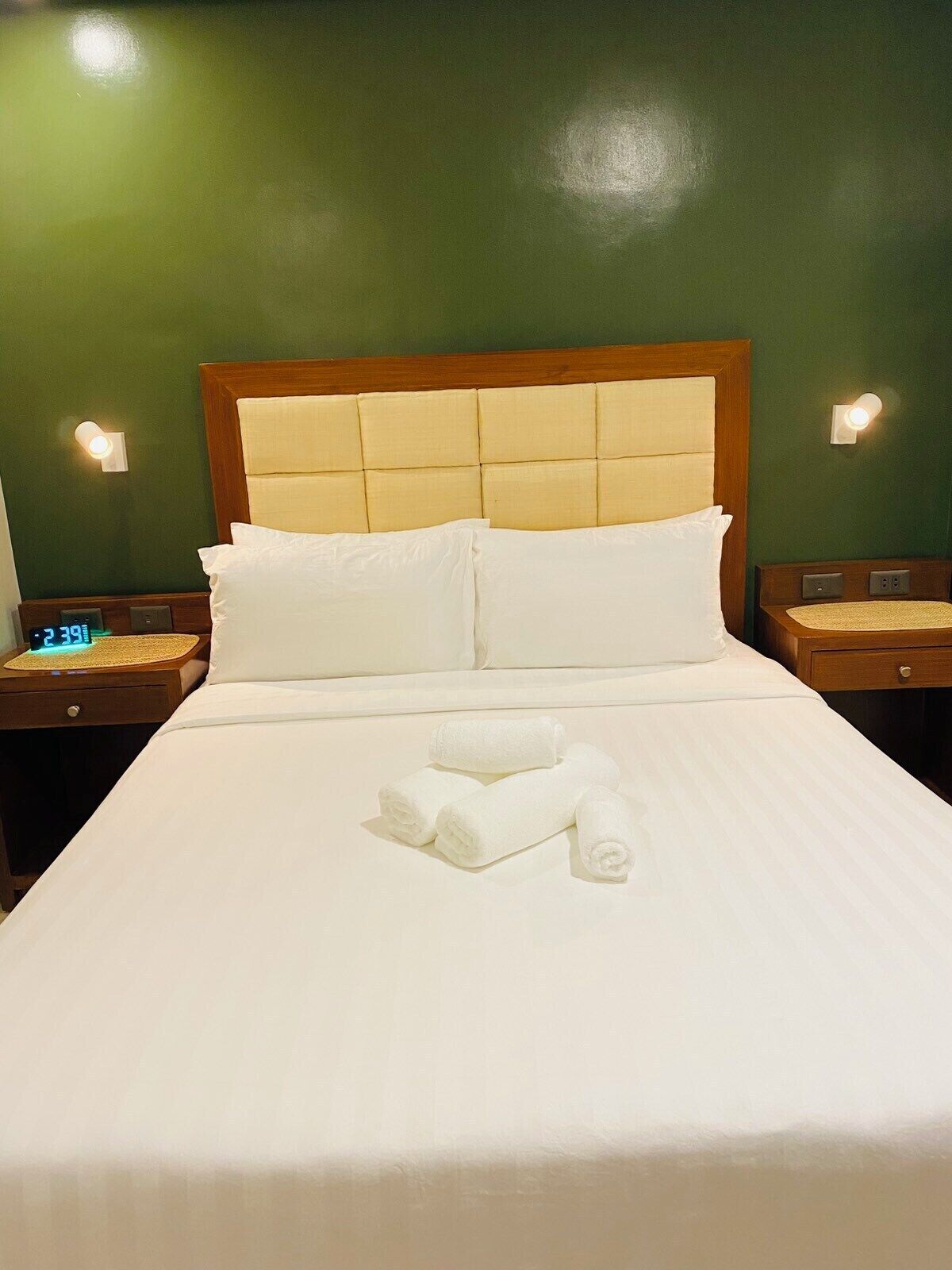 A hotel room with a bed, two bedside tables, and a wall clock.