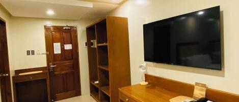 A hotel room with a wooden desk, a television, a chair, and a wardrobe.