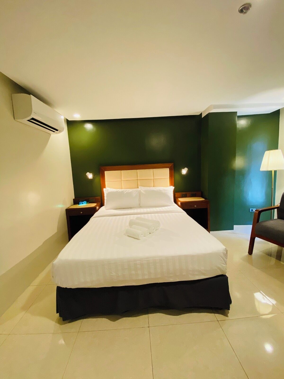A hotel room with a bed, nightstands, an air conditioner, a lamp, and a chair.