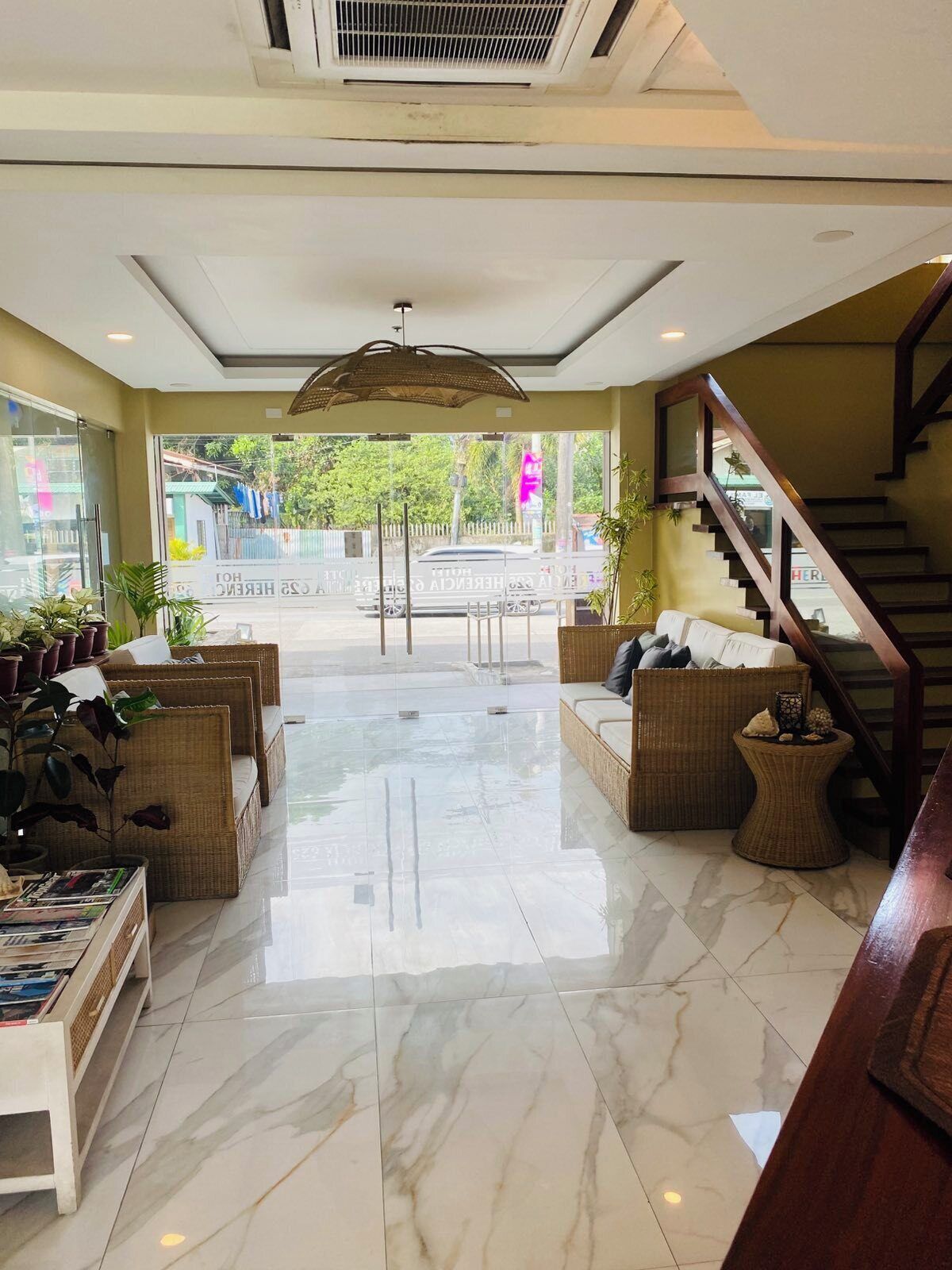 A hotel lobby with a central seating area, a staircase, and a view of the street outside.