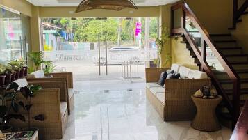 A hotel lobby with a central seating area, a staircase, and a view of the street outside.