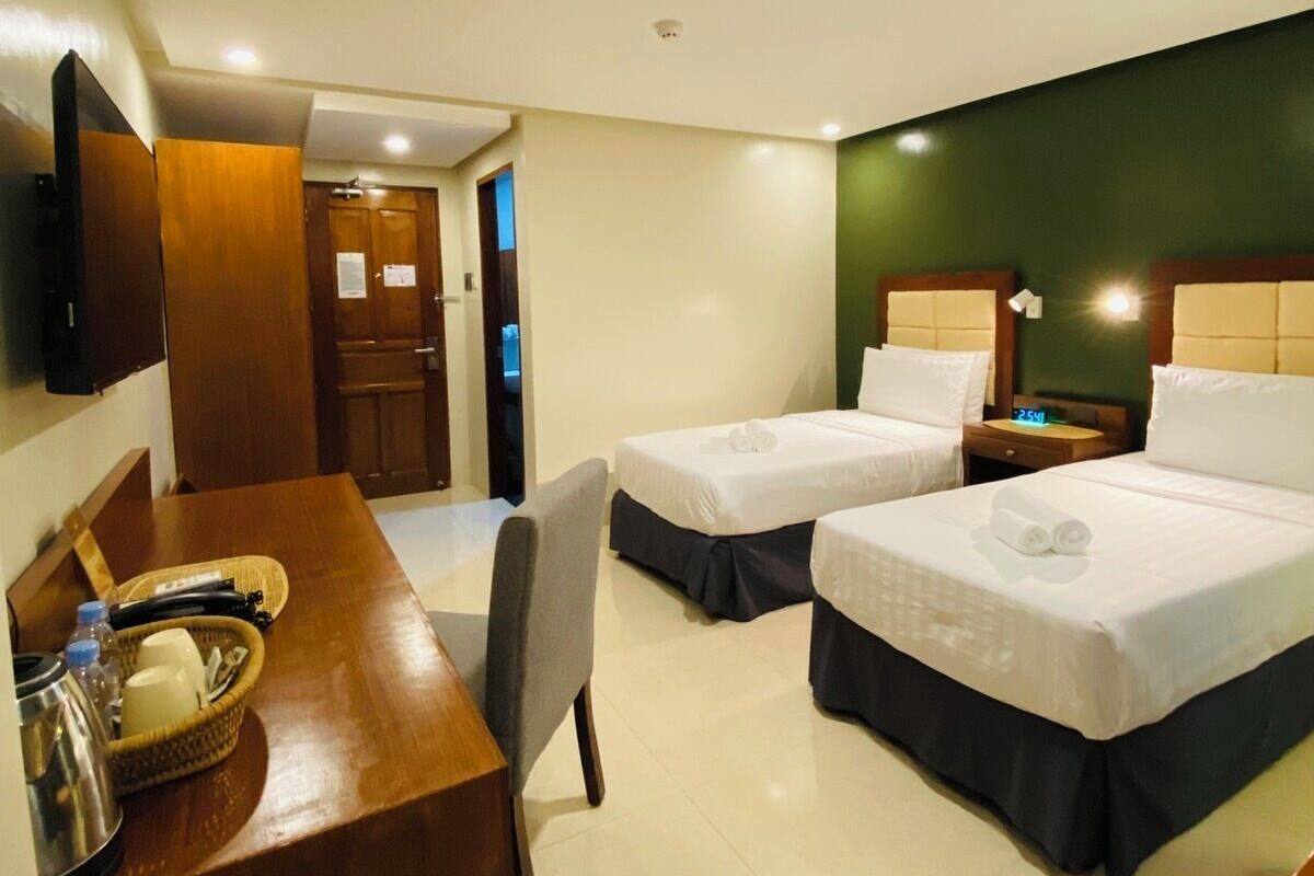 Une chambre d’hôtel avec deux lits, un bureau, une chaise, une télévision et une porte donnant sur une autre pièce.