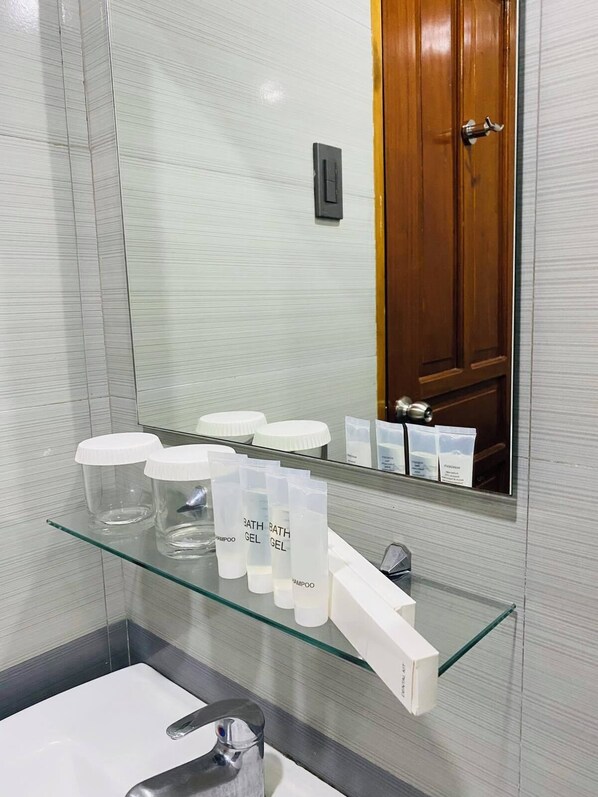 A bathroom with a glass shelf holding toiletries, a mirror, and a wooden door in the background.