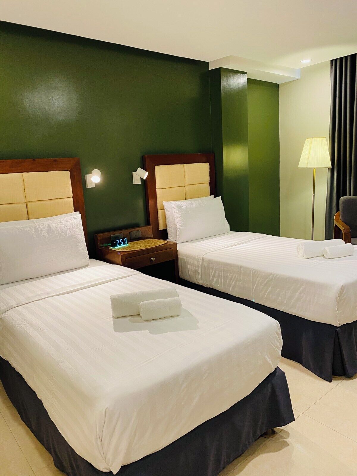 Habitación de hotel con dos camas, una mesita de noche, una lámpara y un reloj.