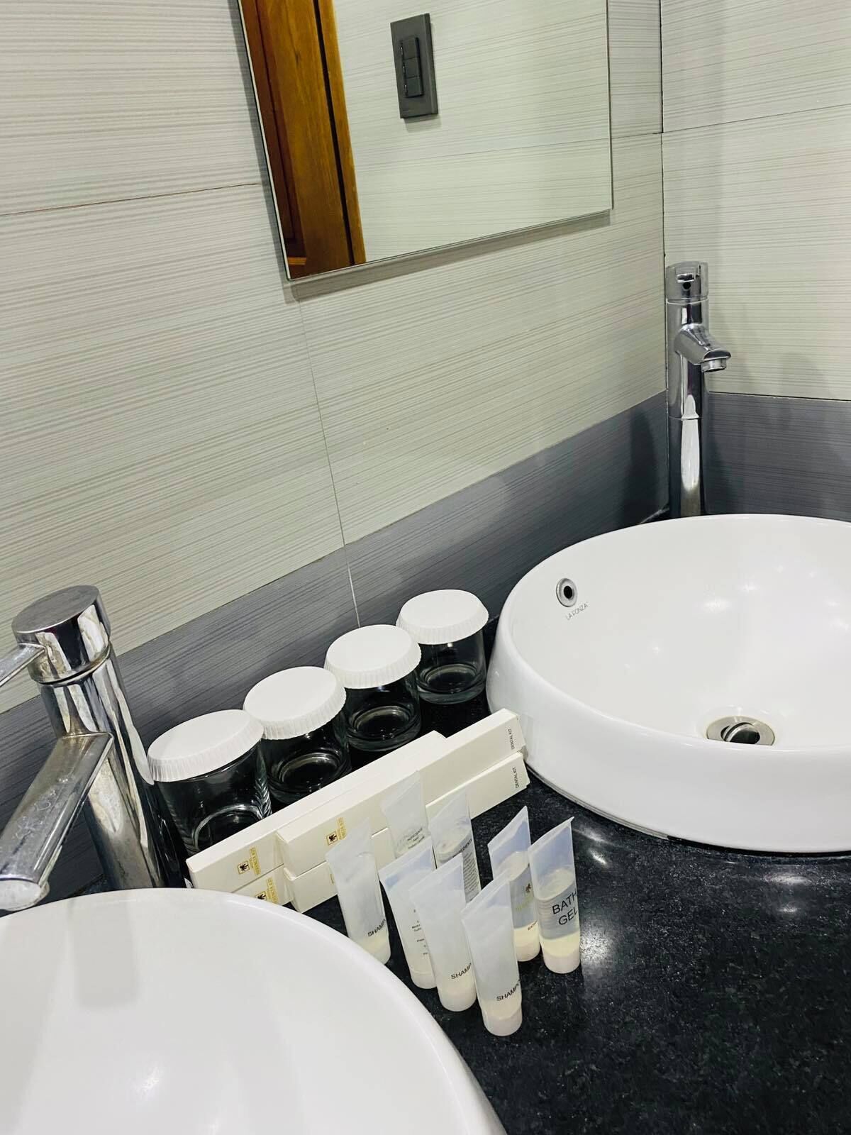 Un baño con lavamanos blanco, espejo, grifo y dispensador de artículos de aseo.