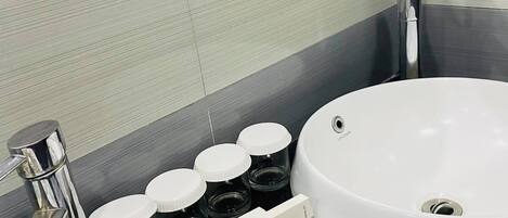 Un baño con lavamanos blanco, espejo, grifo y dispensador de artículos de aseo.