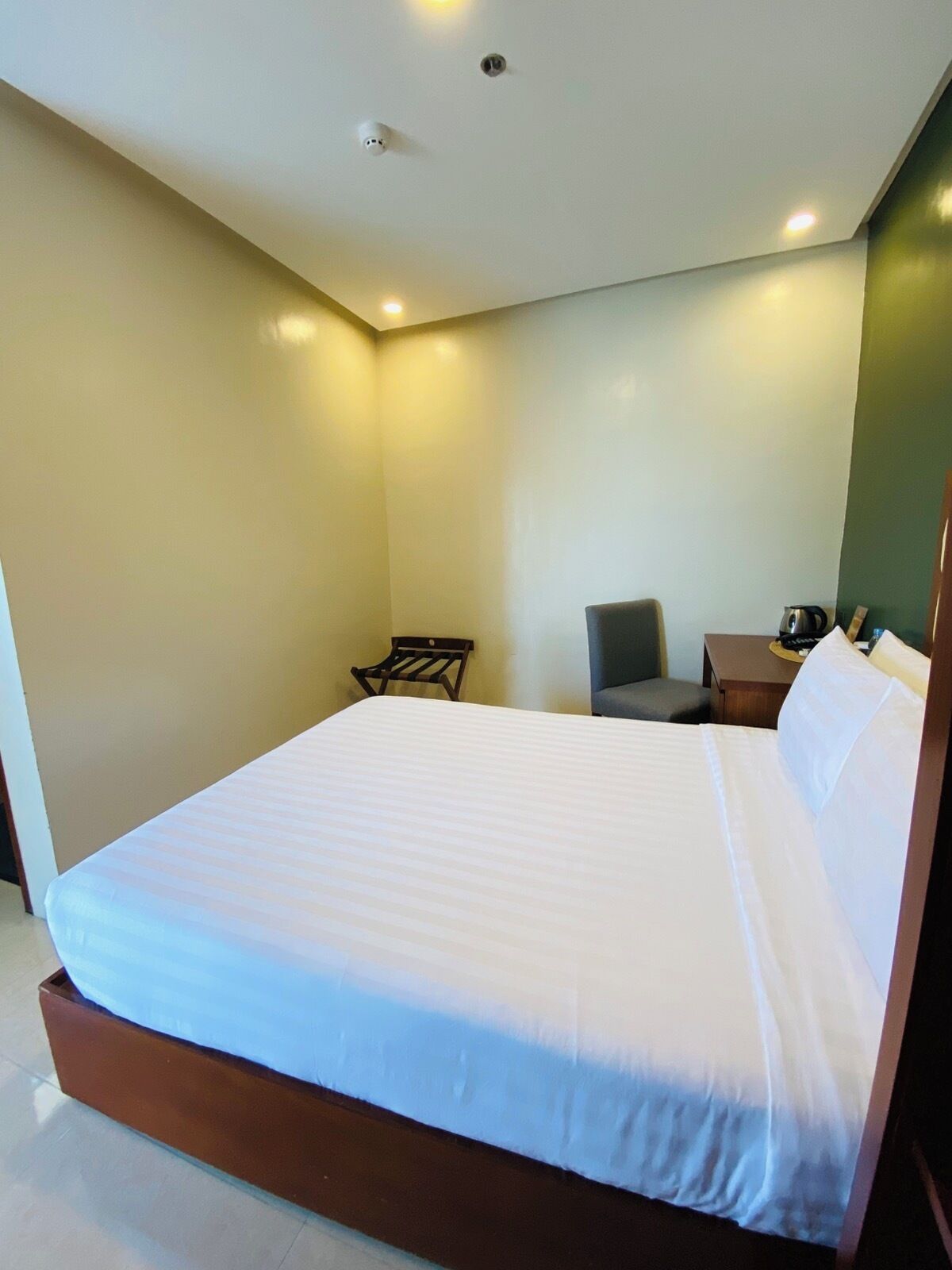 Una habitación de hotel moderna con una cama grande, un escritorio pequeño, una silla y una mesita de noche.