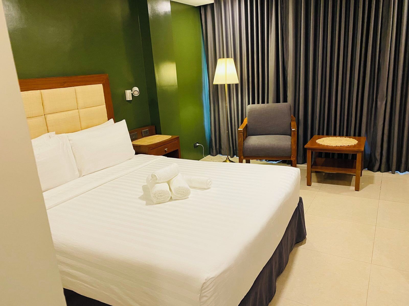 A hotel room with a large bed, a chair, a small table, and a lamp.