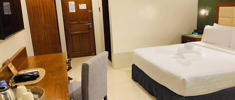 A hotel room with a bed, a desk with a chair, a television, and an air conditioning unit.