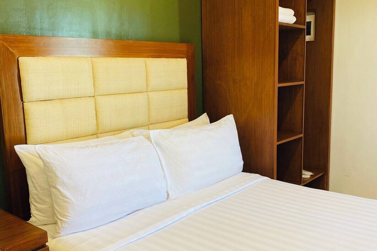Un lit bien fait, avec une tête de lit en bois, une table de chevet en bois et une armoire intégrée dotée d’étagères.