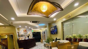 A hotel lobby with a reception desk, wicker furniture, marble flooring, and a ceiling light fixture. - Hotel Herencia 625 (Daraga)