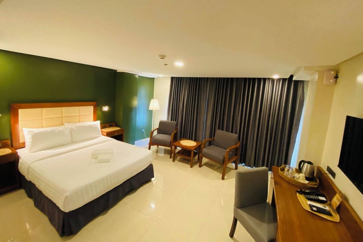 Une chambre d’hôtel avec un grand lit, deux fauteuils, une petite table, un bureau avec un plateau et un téléviseur.
