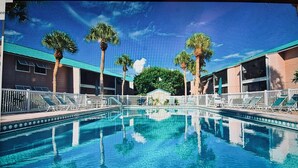 A swimming pool with clear blue water, surrounded by palm trees and a building with a green roof. - Siesta Key Escape: Spacious 2BR /2BA Near Beach + Dining (Siesta Key)
