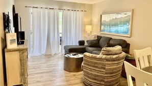 A living room with a grey sofa, a round woven chair, a coffee table, and a painting on the wall. - Siesta Key Escape: Spacious 2BR /2BA Near Beach + Dining (Siesta Key)