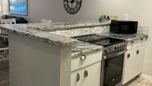 A modern kitchen with a central island, stainless steel appliances, and a clock on the wall. - Siesta Key Escape: Spacious 2BR /2BA Near Beach + Dining (Siesta Key)