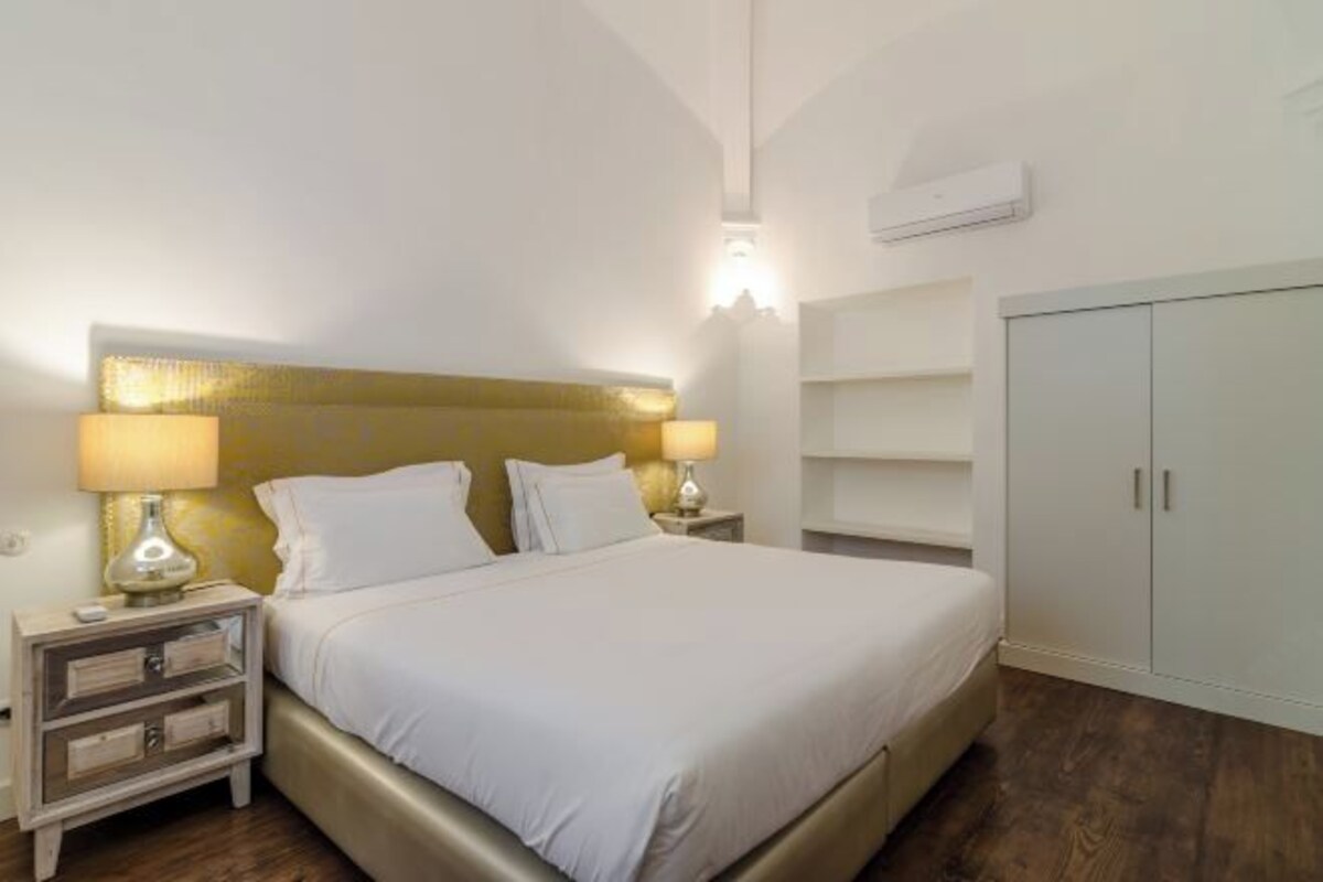 Un dormitorio ordenado con cama, lámparas de noche, armario y aire acondicionado de pared.