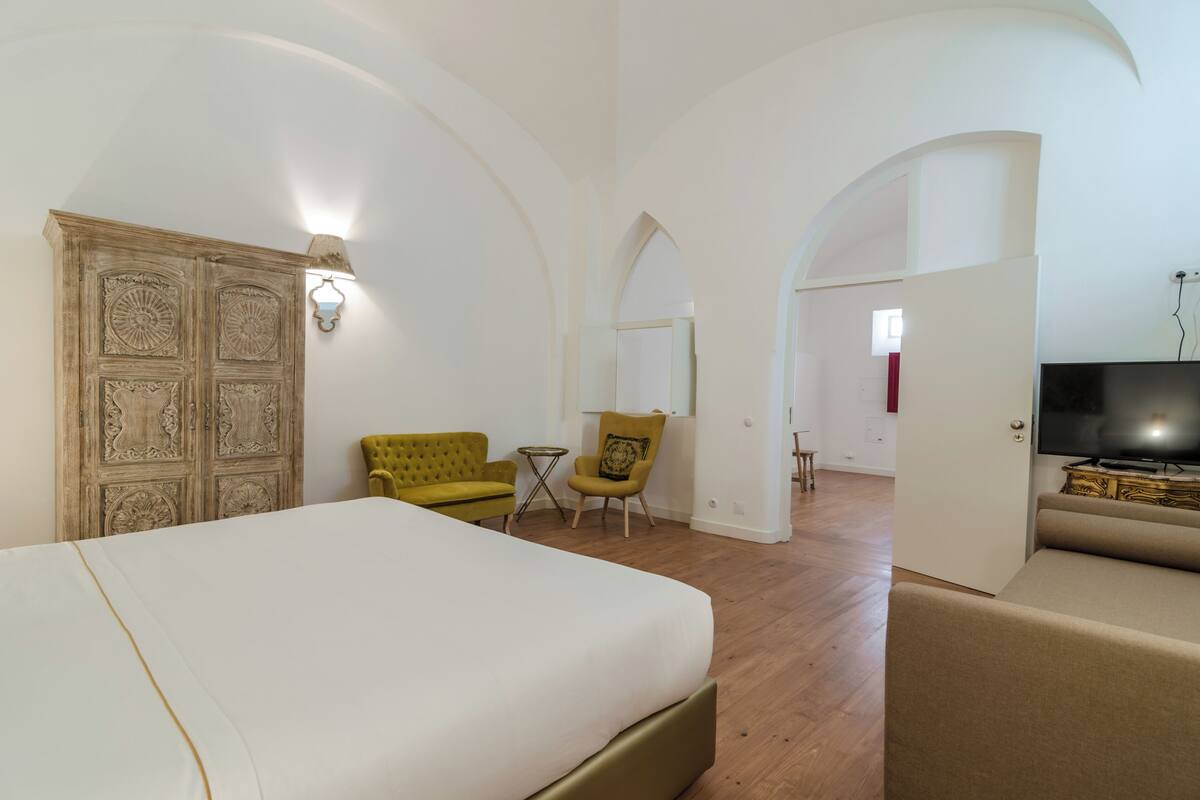 A hotel room with a large bed, a yellow armchair, a small table, and a television.