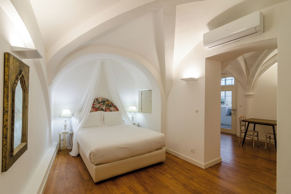 Un dormitorio con una cama grande, una mesita de noche, una lámpara, un espejo y un techo abovedado.