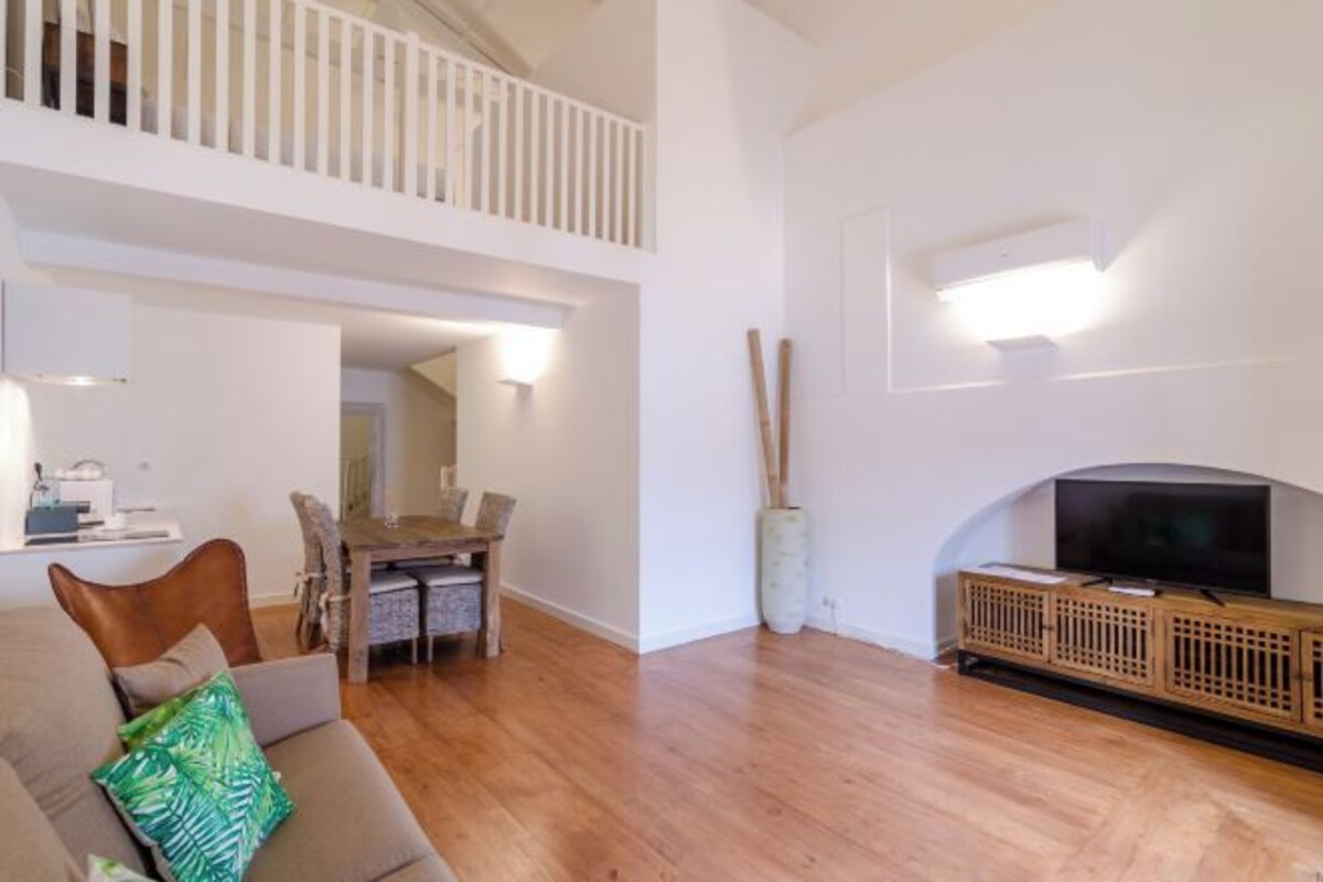 Una sala de estar moderna con techo alto, un comedor con mesa y sillas de madera, y un televisor sobre un mueble de madera.