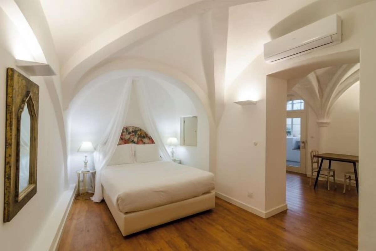 A bedroom with a large bed, a canopy, a wooden floor, and a dining area with a table and chairs.