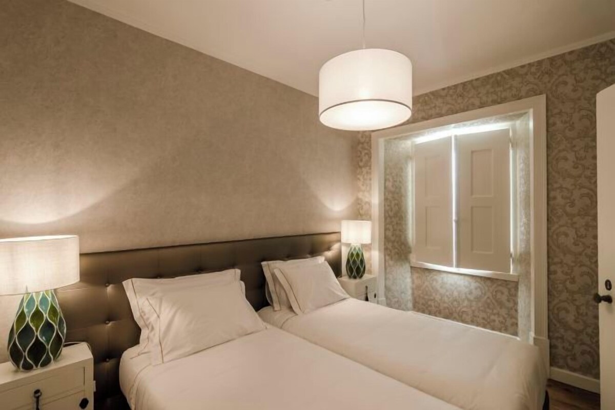 A bedroom with a large bed, two bedside tables with lamps, a headboard, and a door with a mirror.