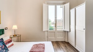 A hotel room with a bed, a nightstand with a lamp, a door leading to a balcony, and a wardrobe. - AwesHome - Pisa Park View Apartment (Pisa)