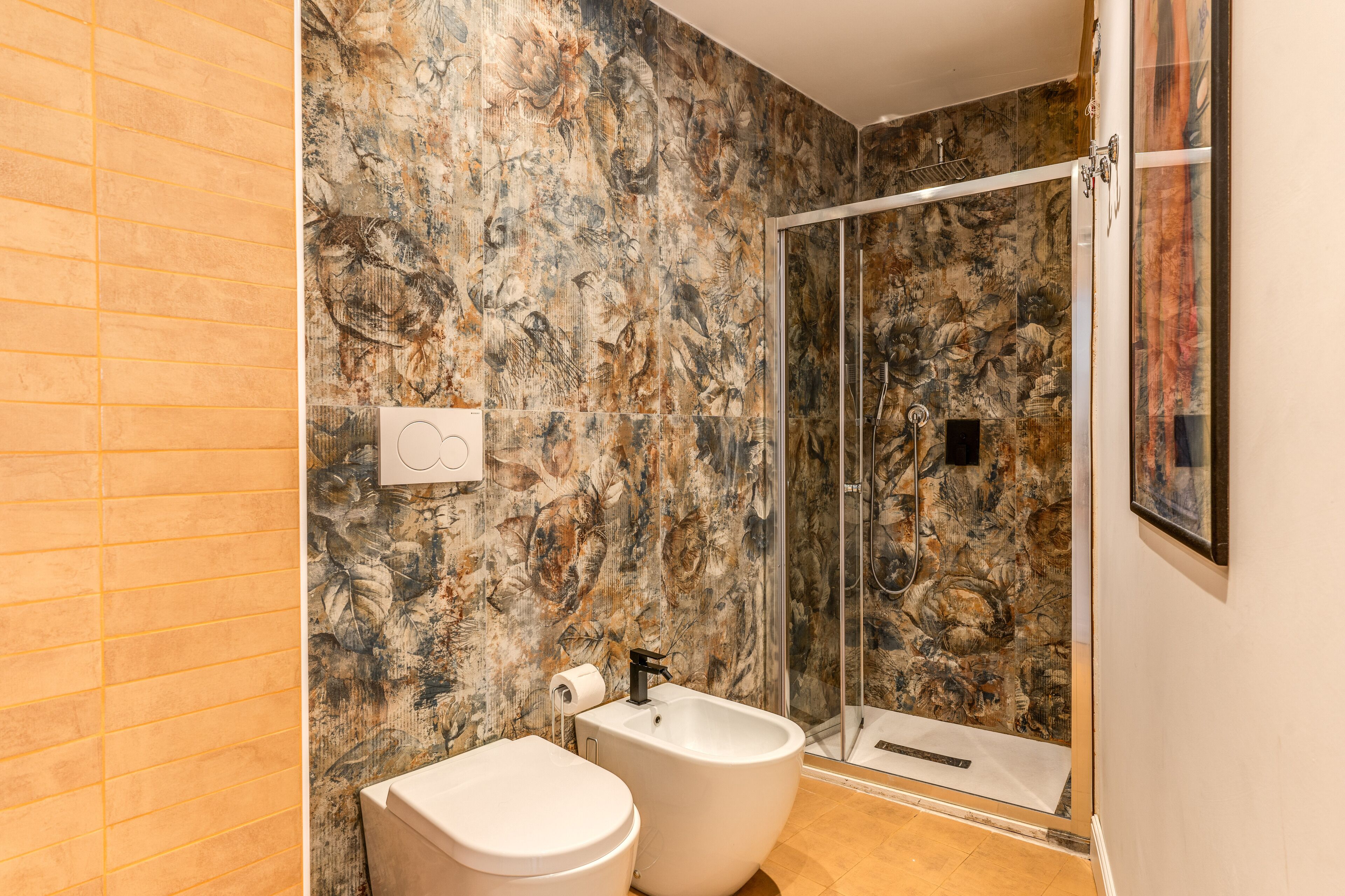 A bathroom with a marble wall, a bidet, a toilet, and a glass shower enclosure.