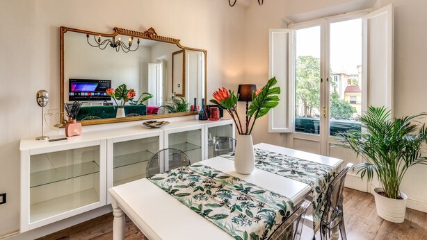 A modern dining area with a white table, a large mirror, and a potted plant. - AwesHome - Pisa Park View Apartment (Pisa)