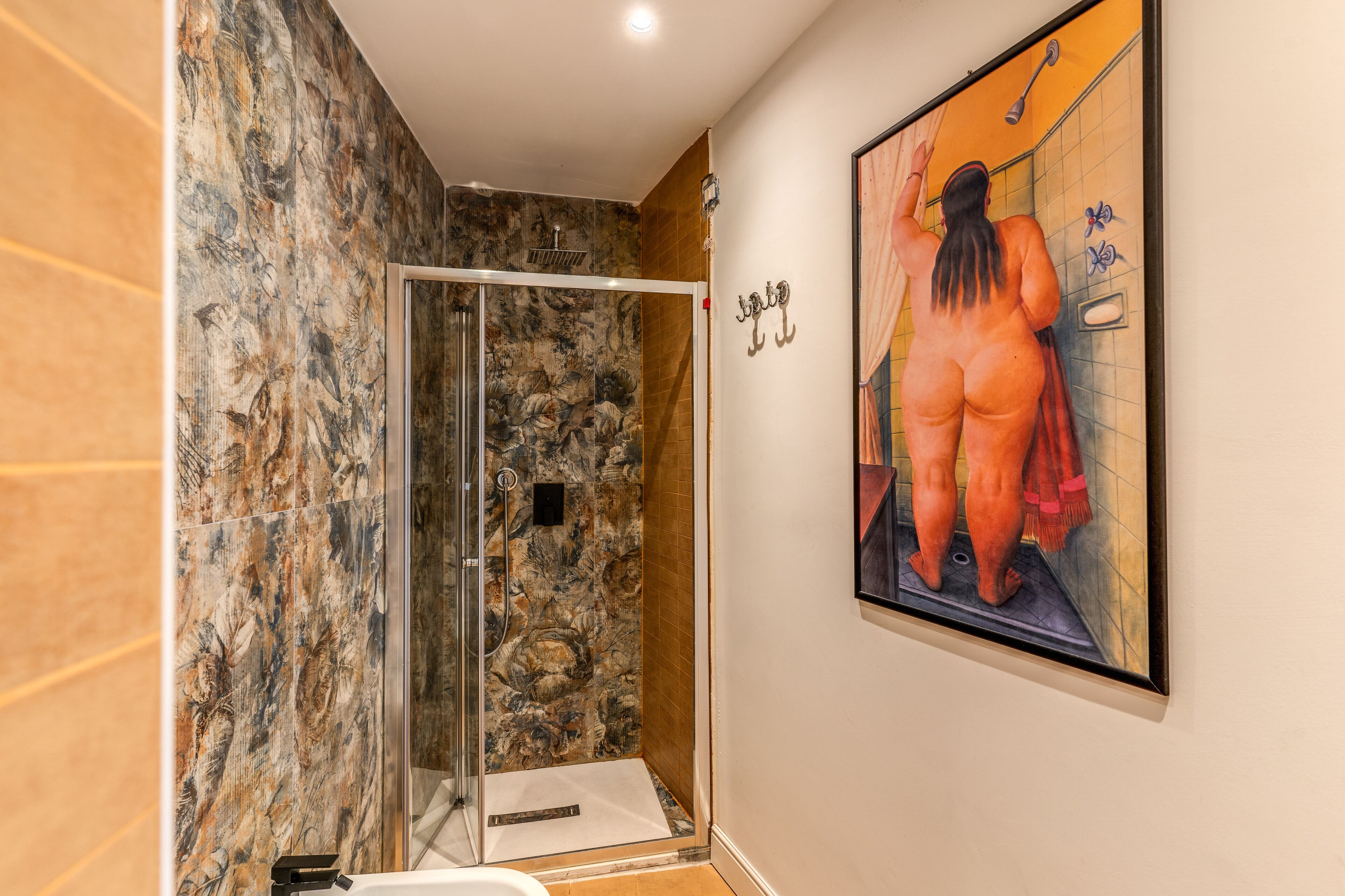 A bathroom with a glass shower enclosure, a marble wall, and a painting of a person.