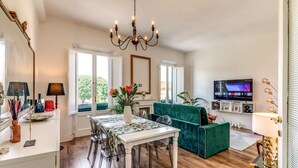 A modern living room with a dining area, a green sofa, a chandelier, and a TV. - AwesHome - Pisa Park View Apartment (Pisa)