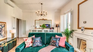A living room with a teal sofa, colorful cushions, a chandelier, a fireplace, and a large mirror. - AwesHome - Pisa Park View Apartment (Pisa)