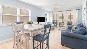 Un coin repas avec une table et des chaises, un téléviseur et une vue sur l’extérieur grâce à une porte-fenêtre coulissante.