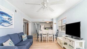 Un salon avec un canapé bleu, un meuble TV blanc et un ventilateur de plafond.