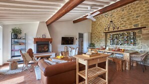 A rustic interior with a stone wall, wooden beams, a fireplace, a dining area, and a wine rack. - La Porcilaia, Pretaccione, Castelnuovo Berardenga, Siena and Chianti (Castelnuovo Berardenga)