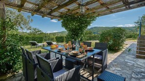 An outdoor dining area with wicker furniture, a table set with plates, bowls, and wine glasses, and a view of the countryside. - La Porcilaia, Pretaccione, Castelnuovo Berardenga, Siena and Chianti (Castelnuovo Berardenga)