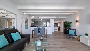 A modern living room with a glass coffee table, a leather sofa, and a dining area with chairs and a kitchen in the background. - RDR299 - 2 Bedroom Frontline Puerto Banús BEST views (Marbella)