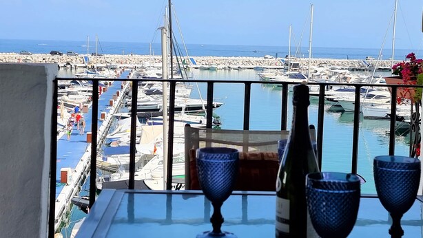 A balcony with a view of a marina, a bottle of wine, and two glasses on the table. - RDR299 - 2 Bedroom Frontline Puerto Banús BEST views (Marbella)