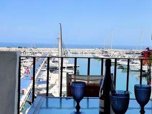 A balcony with a view of a marina, a bottle of wine, and two glasses on the table. - RDR299 - 2 Bedroom Frontline Puerto Banús BEST views (Marbella)