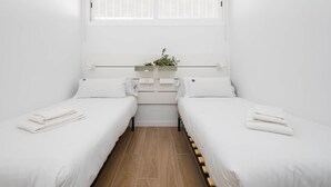 Et enkelt møbleret værelse med to senge, et lille bord med en plante og et vindue med skodder.